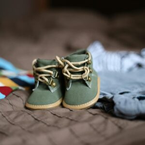 Adorable green baby booties surrounded by colorful clothes, perfect for infant fashion.